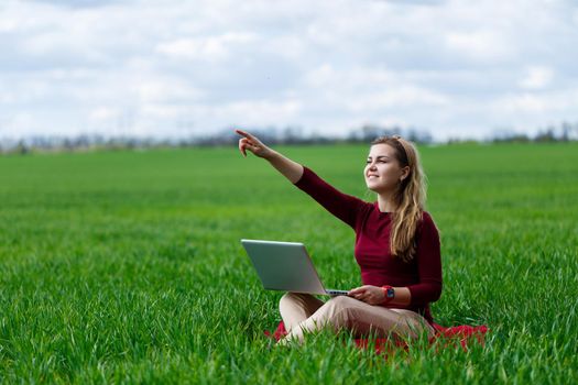Young successful woman is sitting on green grass with a laptop in her hands. Work on the nature. Student girl working in a secluded place. New business ideas