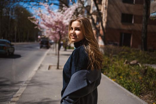 Sakura branches with flowers on a tree on the city streets. Stylish woman girl runs on the street with blooming sakura. Gorgeous fashionable girl outdoors. Sakura tree blossoms.