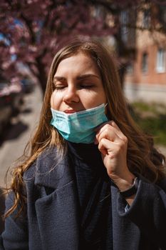 Girl, young woman in a protective sterile medical mask on her face, looking at the camera outdoors, in the spring garden. Air pollution, virus, pandemic coronavirus concept.
