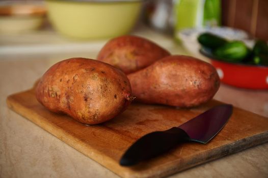 Raw whole sweet potato or batatas on old wooden chopping board. Batatas on wooden surface. Healthy food. Raw organic batatas tubers. Healthy dieting food enriched in minerals and vitamins. Veganism