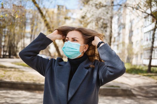 Girl, young woman in a protective sterile medical mask on her face, looking at the camera outdoors, in the spring garden. Air pollution, virus, pandemic coronavirus concept.