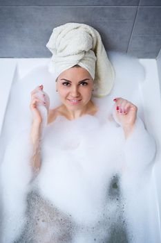 Girl woman with a white towel on her head lies in the bathroom in a white bath. Foam for around. Relax after a hard day. Spa relaxing treatment