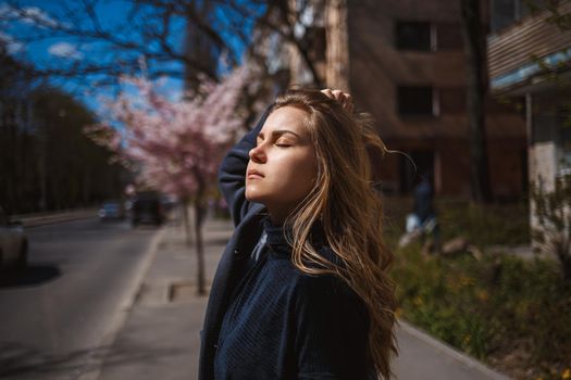 Sakura branches with flowers on a tree on the city streets. Happy woman girl spinning on the street with blooming sakura. Gorgeous fashionable girl outdoors. Sakura tree blossoms.