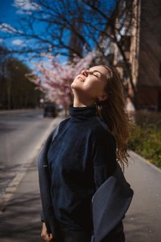 Sakura branches with flowers on a tree on the city streets. Stylish woman girl runs on the street with blooming sakura. Gorgeous fashionable girl outdoors. Sakura tree blossoms.