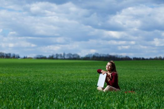 Young successful woman is sitting on green grass with a laptop in her hands. Rest after a good working day. Work on the nature. Student girl working in a secluded place. Workplace in nature