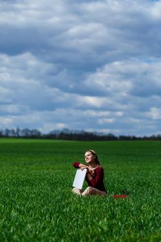 Young successful woman is sitting on green grass with a laptop in her hands. Rest after a good working day. Work on the nature. Student girl working in a secluded place. Workplace in nature