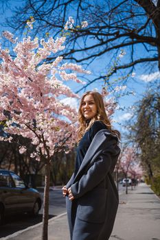 Sakura branches with flowers on a tree on the city streets. Happy woman girl spinning on the street with blooming sakura. Gorgeous fashionable girl outdoors. Sakura tree blossoms.