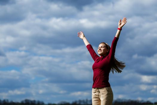 Joyful young girl on a background of the sky with clouds. He raised his hands up and laughed. Happiness in lifestyle. Inspiration in nature. Rest after a good working day.