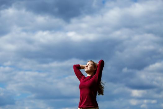 Joyful young girl on a background of the sky with clouds. He raised his hands up and laughed. Happiness in lifestyle. Inspiration in nature. Rest after a good working day.