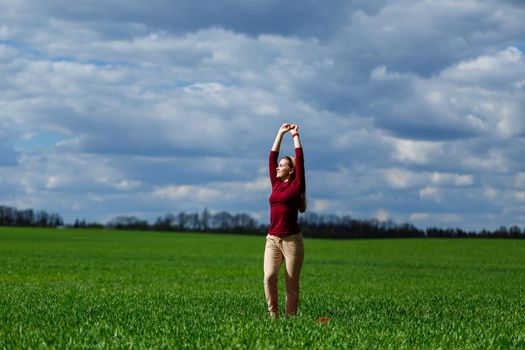 Beautiful young blonde woman stands on green grass in a park. Blue sky with clouds. The girl smiles and enjoys a good day.