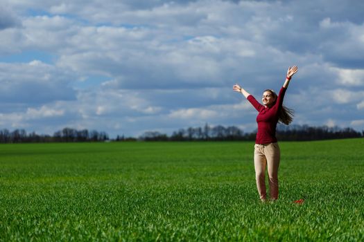 Beautiful young blonde woman stands on green grass in a park. Blue sky with clouds. The girl smiles and enjoys a good day.