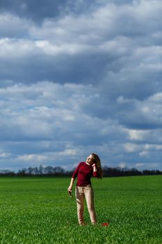Beautiful young blonde woman stands on green grass in a park. Blue sky with clouds. The girl smiles and enjoys a good day.