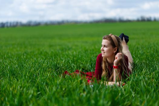 Beautiful young blonde woman is lying on the green grass in the park with a laptop and working. Blue sky with clouds. The girl smiles and enjoys a good day. Work on the nature on a sunny day.