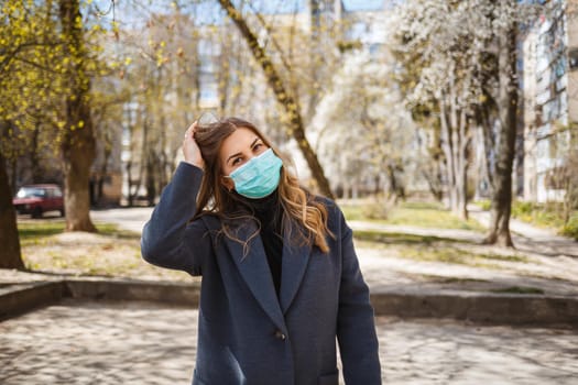 Girl, young woman in a protective sterile medical mask on her face, looking at the camera outdoors, in the spring garden. Air pollution, virus, pandemic coronavirus concept.