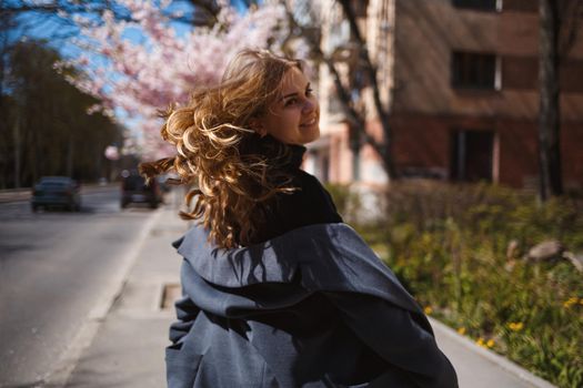 Sakura branches with flowers on a tree on the city streets. Stylish woman girl runs on the street with blooming sakura. Gorgeous fashionable girl outdoors. Sakura tree blossoms.