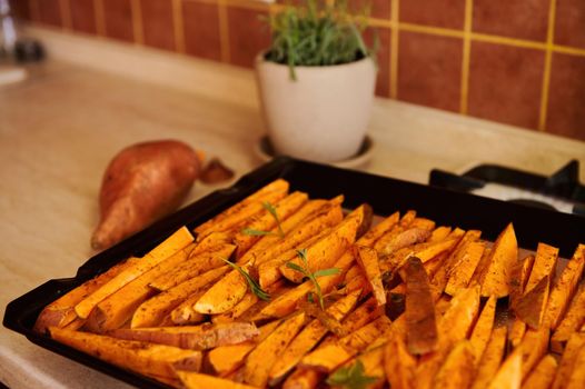 Close-up of baking sheet with wedges of raw organic sweet potato, seasoned with fragrant culinary herbs, before baking in oven. Cooking homemade delicious healthy vegan meal for dinner - fried batata