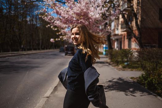 Sakura branches with flowers on a tree on the city streets. Stylish woman girl runs on the street with blooming sakura. Gorgeous fashionable girl outdoors. Sakura tree blossoms.