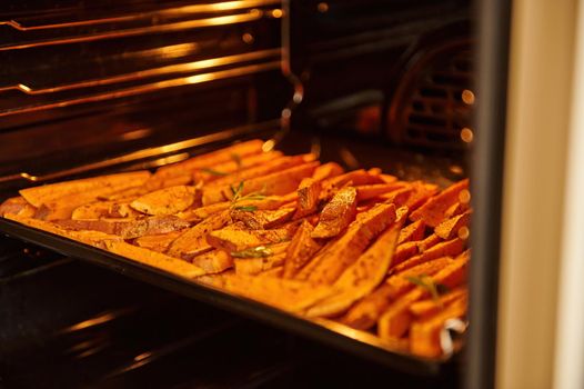 Close-up of sliced sweet potatoes, wedges of batata on a baking sheet, baked and fried with spices and herb in the oven. Healthy food. Veganism and vegetarianism.