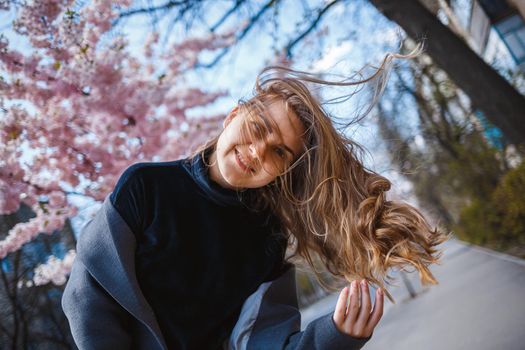 Sakura branches with flowers on a tree on the city streets. Happy woman girl spinning on the street with blooming sakura. Gorgeous fashionable girl outdoors. Sakura tree blossoms.