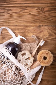 Fishnet shopping bag with ethical eco-friendly cleaning household products: sisal brush, natural luffa, bamboo toothbrush, organic soap in bottle, wooden pins. Conscious consumption concept.