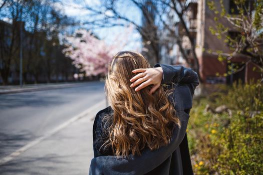 Sakura branches with flowers on a tree on the city streets. Happy woman girl spinning on the street with blooming sakura. Gorgeous fashionable girl outdoors. Sakura tree blossoms.
