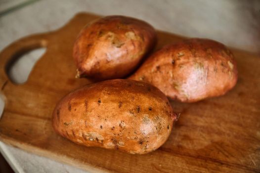 Raw whole sweet potato or batatas on old wooden cutting board. Batatas on wooden surface. Healthy food. Raw organic batatas tubers. Healthy dieting food enriched in minerals and vitamins. Veganism