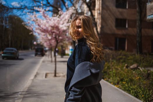 Sakura branches with flowers on a tree on the city streets. Stylish woman girl runs on the street with blooming sakura. Gorgeous fashionable girl outdoors. Sakura tree blossoms.