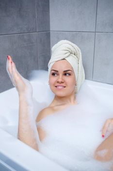 Woman girl with a white towel on her head lies in a white bath. Full bubble bath. Relax after a hard day. Relaxing spa treatments