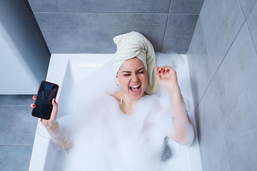 Beautiful young woman listening to music and singing while taking a bath at home. Relax after a hard day. Spa relaxing procedure.