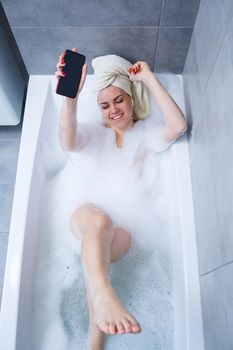 Beautiful young woman listens to music with headphones and sings while taking a bath at home. Relax after a hard day. Relaxing spa treatment.