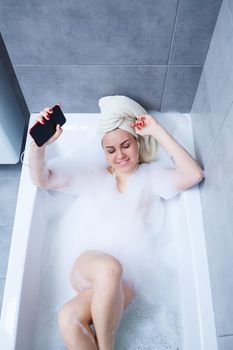 Beautiful young woman listening to music and singing while taking a bath at home. Relax after a hard day. Spa relaxing procedure.
