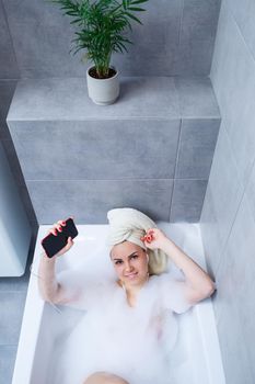 Beautiful young woman listens to music with headphones and sings while taking a bath at home. Relax after a hard day. Relaxing spa treatment.