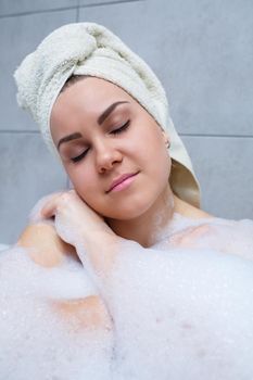Girl woman with a white towel on her head lies in the bathroom in a white bath. Foam for around. Relax after a hard day. Spa relaxing treatment