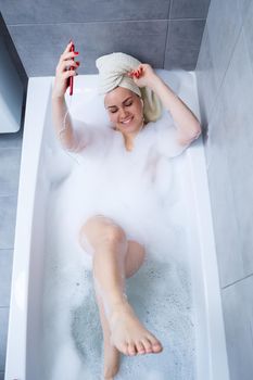 Beautiful young woman listening to music and singing while taking a bath at home. Relax after a hard day. Spa relaxing procedure.