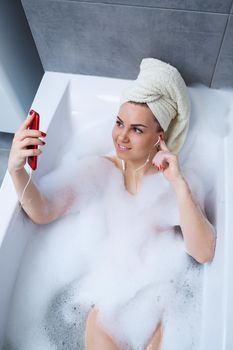 Beautiful young woman listening to music and singing while taking a bath at home. Relax after a hard day. Spa relaxing procedure.