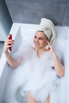 Beautiful young woman listening to music and singing while taking a bath at home. Relax after a hard day. Spa relaxing procedure.