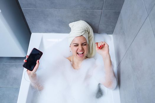 Beautiful young woman listening to music and singing while taking a bath at home. Relax after a hard day. Spa relaxing procedure.