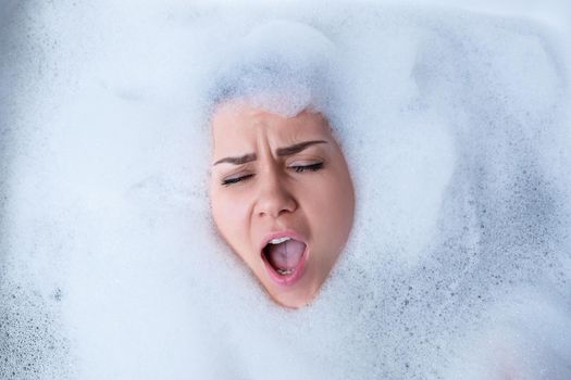 Closeup portrait of a girl in a bathtub and white foam around her face. Different emotions, grimaces, woman smile