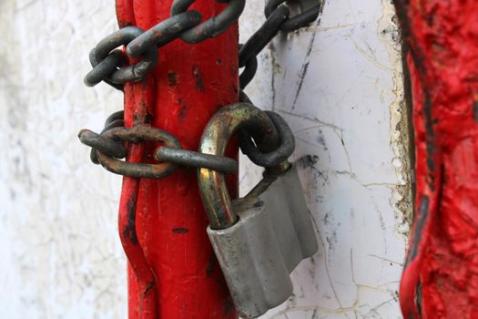 An old padlock on a rusty chain wrapped around red pipes.