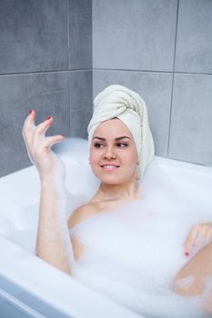 Girl woman with a white towel on her head lies in the bathroom in a white bath. Foam for around. Relax after a hard day. Spa relaxing treatment