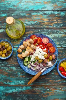 Greek meat souvlaki and mediterranean salad with vegetables, feta cheese on plate on rustic wooden background from above, with olive oil in bottle and assorted traditional appetizers of Greece