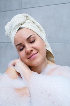 Girl woman with a white towel on her head lies in the bathroom in a white bath. Foam for around. Relax after a hard day. Spa relaxing treatment