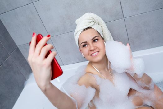 Beautiful young woman listening to music and singing while taking a bath at home. Relax after a hard day. Spa relaxing procedure.