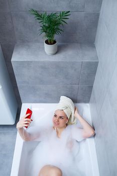 Beautiful young woman listens to music with headphones and sings while taking a bath at home. Relax after a hard day. Relaxing spa treatment.