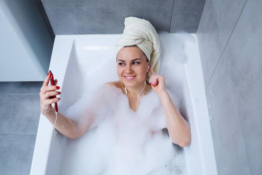 Beautiful young woman listening to music and singing while taking a bath at home. Relax after a hard day. Spa relaxing procedure.