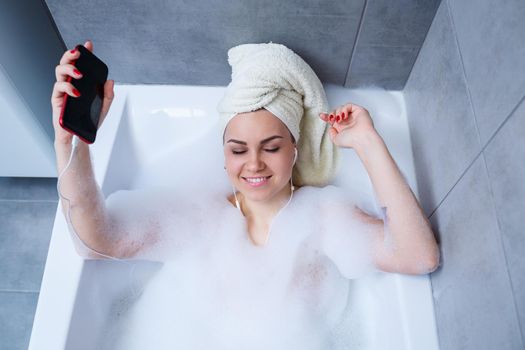 Beautiful young woman listening to music and singing while taking a bath at home. Relax after a hard day. Spa relaxing procedure.