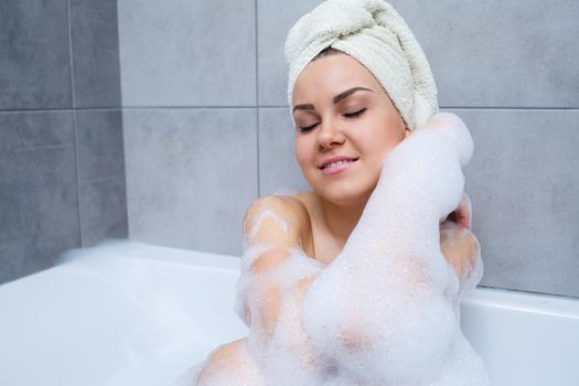 Girl woman with a white towel on her head lies in the bathroom in a white bath. Foam for around. Relax after a hard day. Spa relaxing treatment