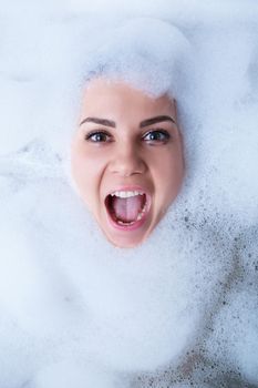 Closeup portrait of a girl in a bathtub and white foam around her face. Different emotions, grimaces, woman smile