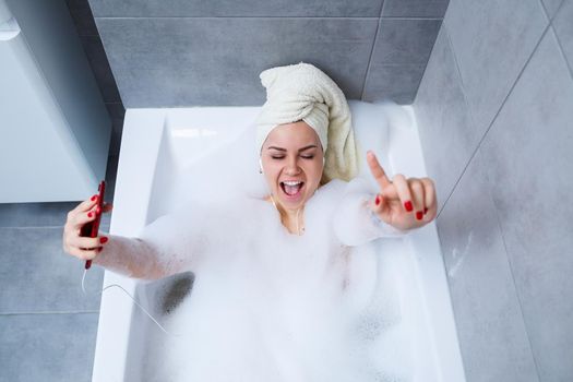 Beautiful young woman listening to music and singing while taking a bath at home. Relax after a hard day. Spa relaxing procedure.
