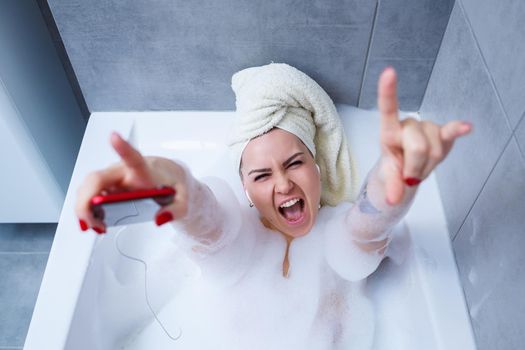 Beautiful young woman listening to music and singing while taking a bath at home. Relax after a hard day. Spa relaxing procedure.
